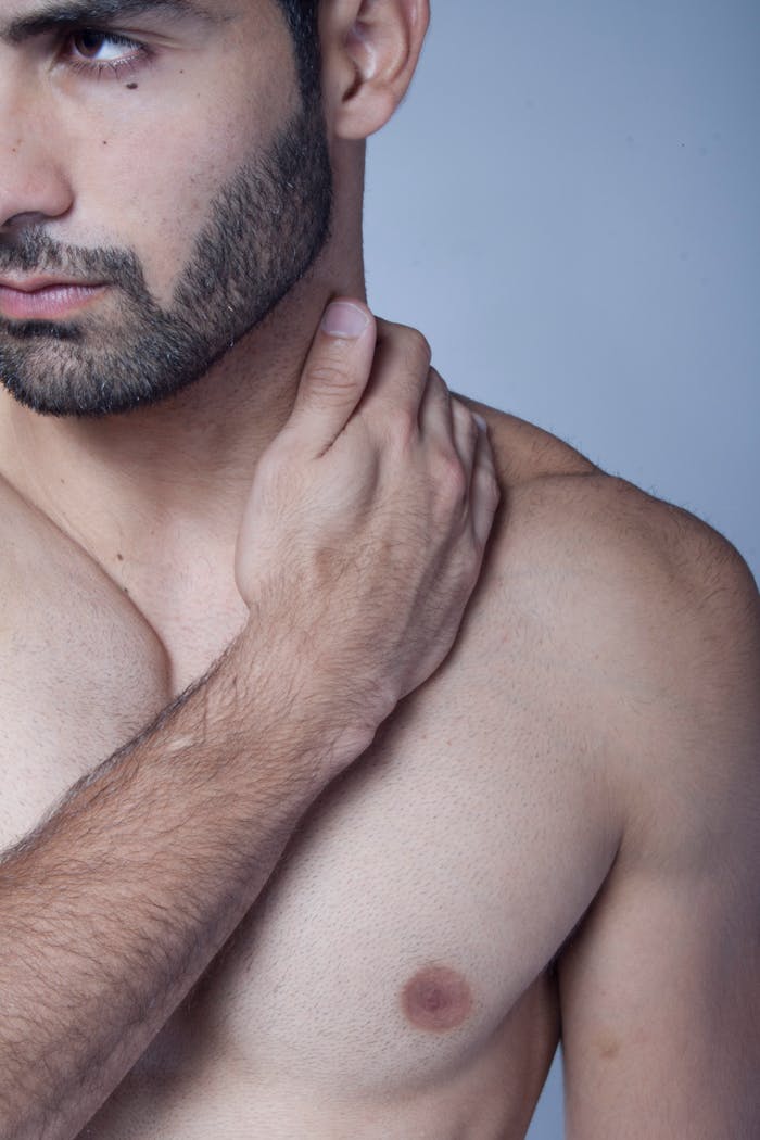Close-up of a topless bearded man gently holding his neck, emphasizing masculinity and self-awareness.